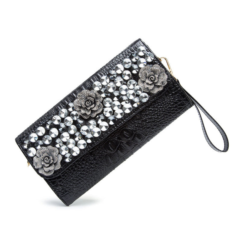 Angled view of the black textured clutch with wrist strap and embellished flap