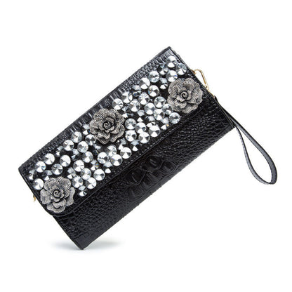 Angled view of the black textured clutch with wrist strap and embellished flap