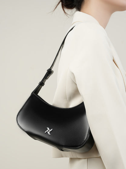 Black leather crescent shoulder bag worn on shoulder with white blazer