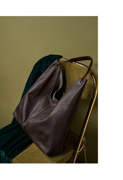 Brown hobo tote bag styled on a green velvet chair against olive wall