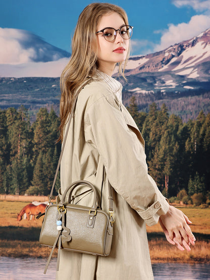 Model in a beige trench coat wearing a gray leather pillow bag on crossbody outdoors