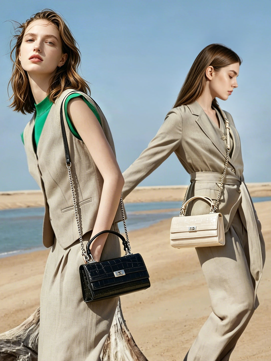 Two models walking on a sandy beach, one carrying black bag and one carrying cream white bag by the top handle