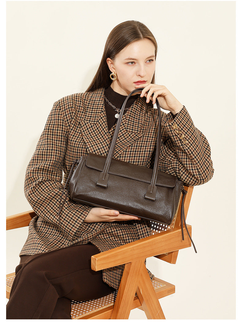 Model seated in houndstooth coat holding dark brown cowhide leather shoulder bag