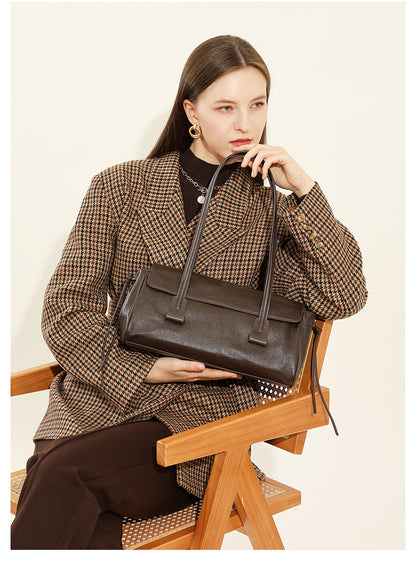 Model seated in houndstooth coat holding dark brown cowhide leather shoulder bag