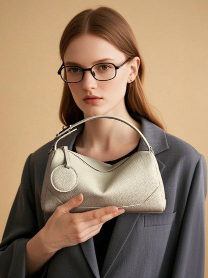 Model in glasses holding elephant gray mini Boston bag against gray blazer