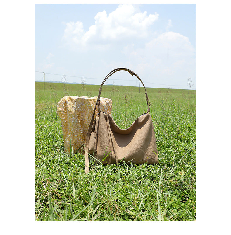 Gray cowhide leather hobo bag with adjustable strap standing on grass