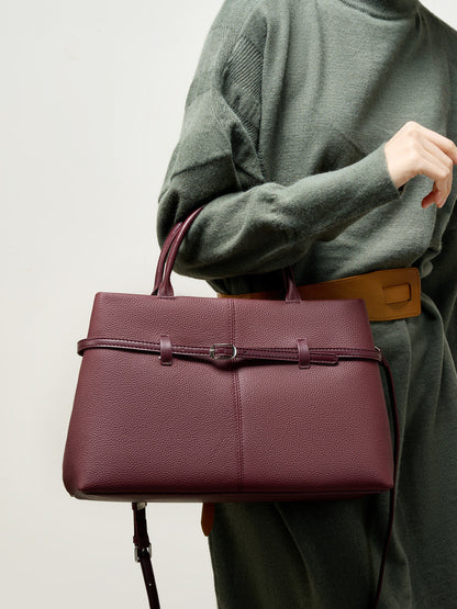 Model in green sweater holding wine red cowhide tote at waist