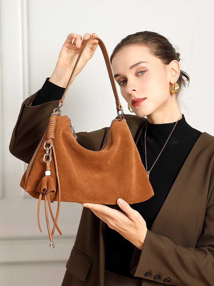 Model holding brown nubuck cowhide tote showing tassel and zip closure
