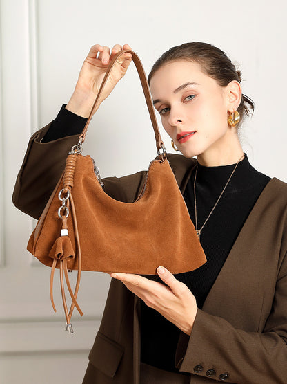 Model holding brown nubuck cowhide tote showing tassel and zip closure
