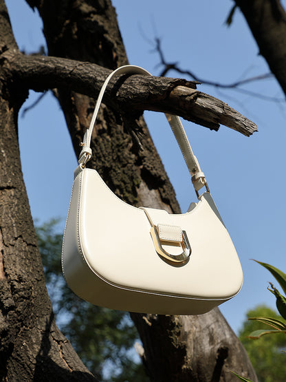 Cream white shoulder bag hanging on tree branch in sunlight