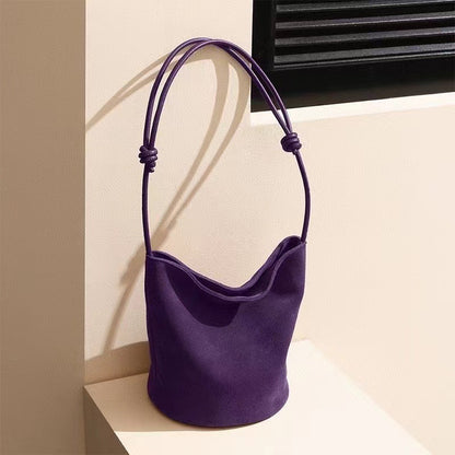 Purple leather bucket shoulder bag on a display surface
