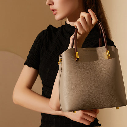 Gray bucket bag carried by the top handles against a black top