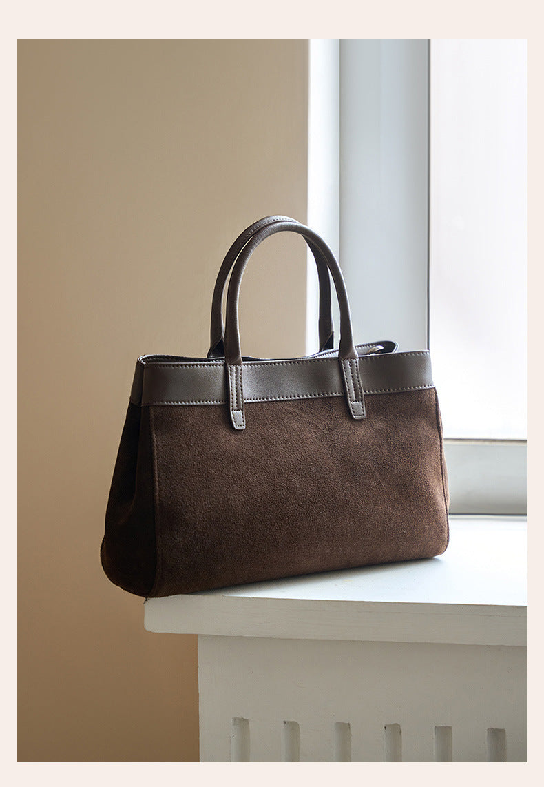 Coffee suede cowhide handbag with twin top handles displayed on a ledge