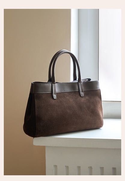 Coffee suede cowhide handbag with twin top handles displayed on a ledge