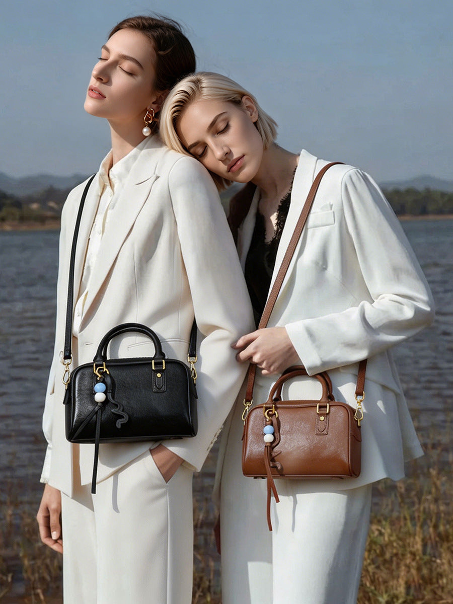 Two models wearing black and brown leather pillow bags in neutral blazers by the water