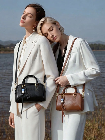 Two models wearing black and brown leather pillow bags in neutral blazers by the water