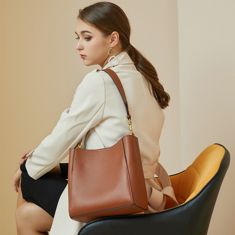 Model wearing tan cowhide leather bucket tote as shoulder bag with trench coat