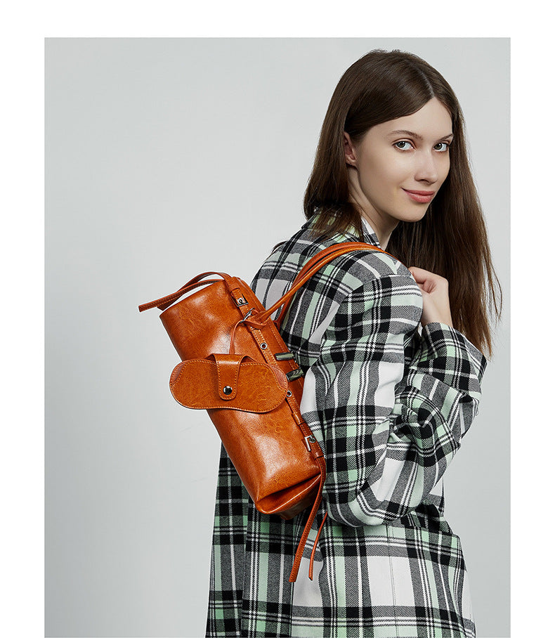 Model in plaid coat with tan barrel bag tucked under arm