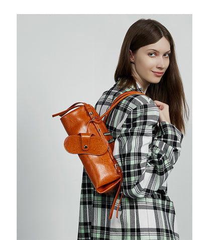 Model in plaid coat with tan barrel bag tucked under arm