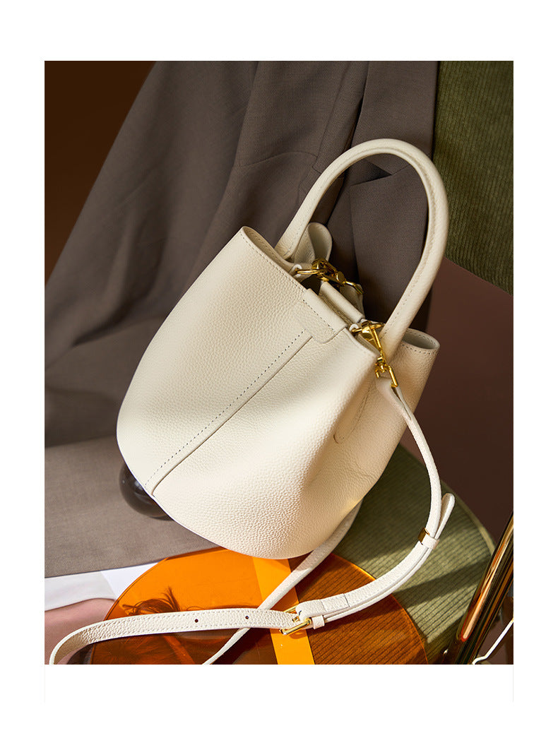 Off-white bucket bag styled on chair with crossbody strap visible