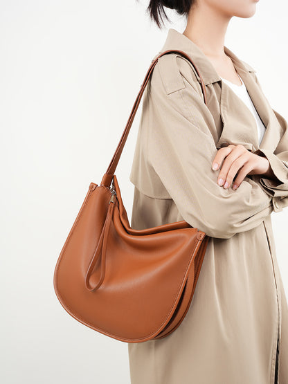 Tan leather hobo bag worn on shoulder by model in trench coat