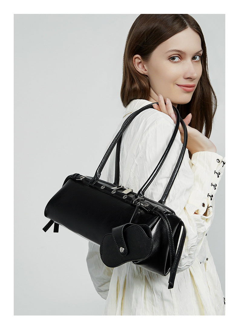 Side view of model carrying black leather barrel tote on shoulder
