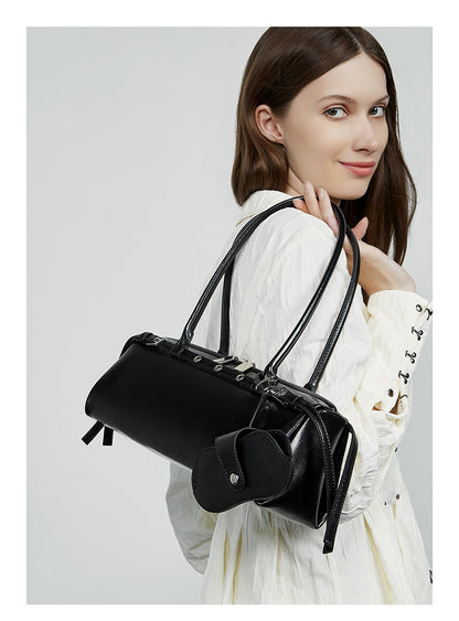 Side view of model carrying black leather barrel tote on shoulder
