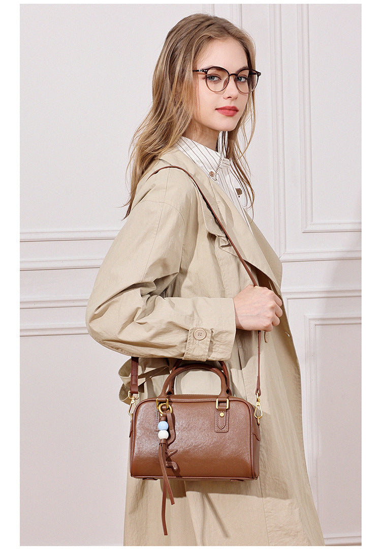 Model in a beige trench coat wearing a caramel brown leather pillow crossbody bag