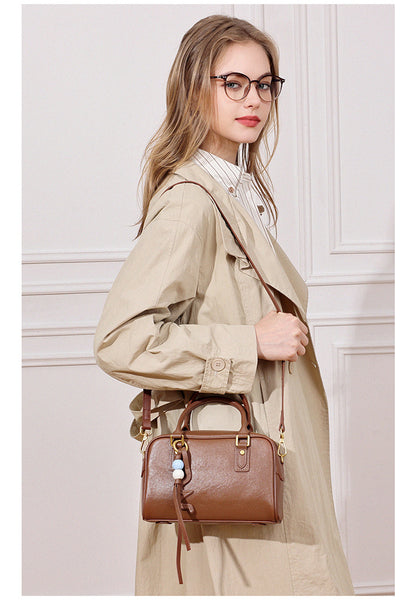 Model in a beige trench coat wearing a caramel brown leather pillow crossbody bag