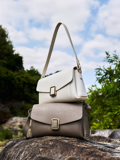 Cream white and gray cowhide leather crossbody bags stacked on outdoor rock