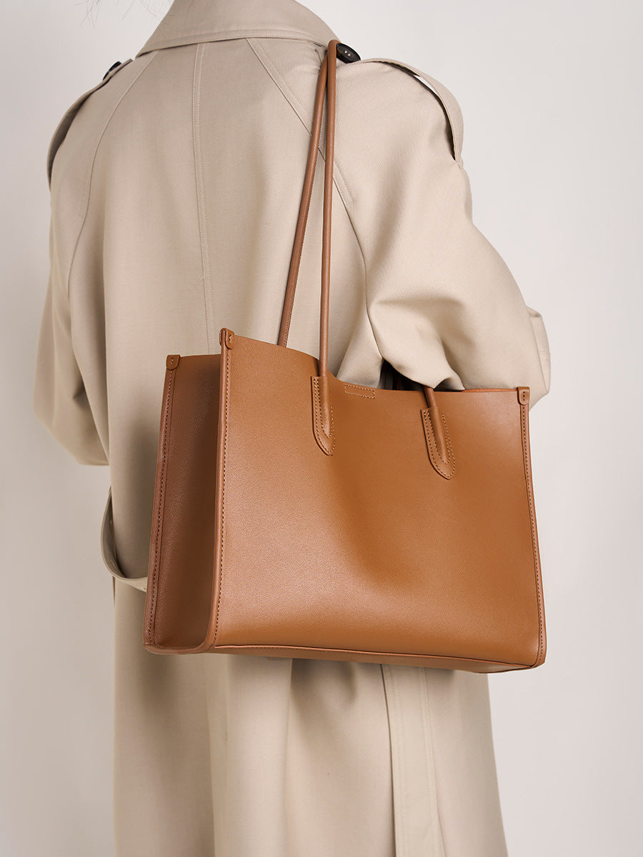 Golden brown leather tote bag carried over the shoulder with trench coat
