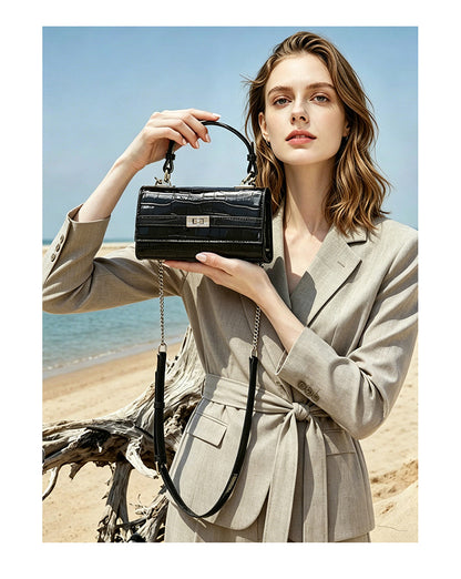 Model holding the black croco-embossed bag at chest height in a relaxed pose by the sea