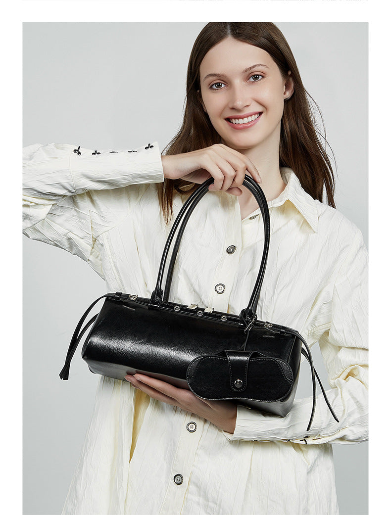 Model in cream button-up holding black leather barrel bag by top handles