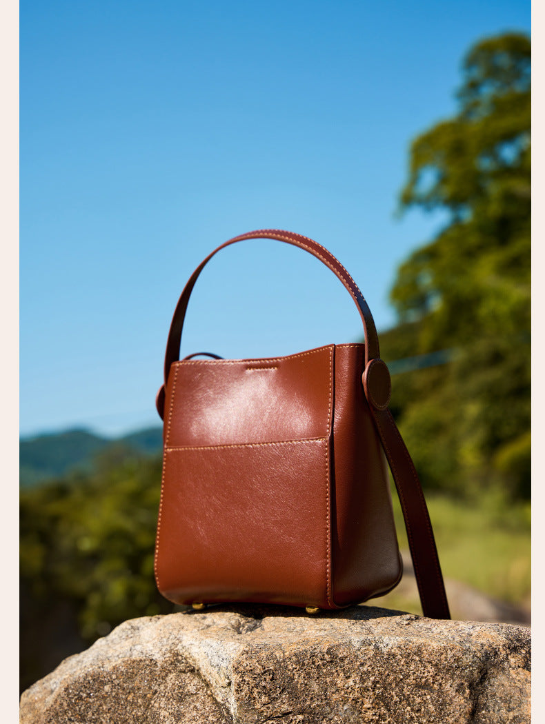 Brown cowhide bucket bag styled outdoors on a stone under blue sky