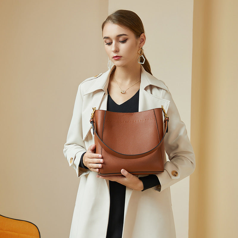 Model holding tan leather bucket bag in front while wearing cream trench coat