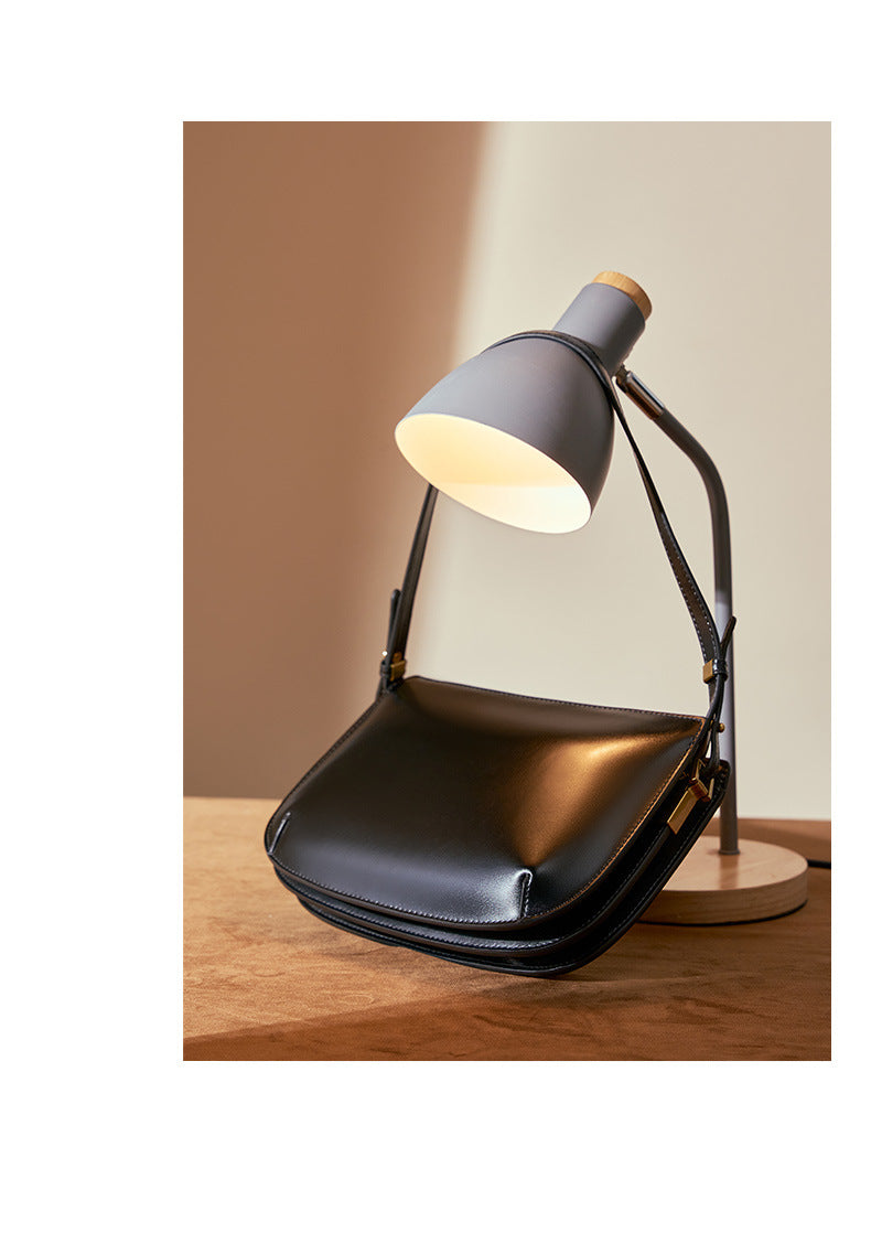 Black leather underarm bag hanging from a gray desk lamp, showcasing the silhouette