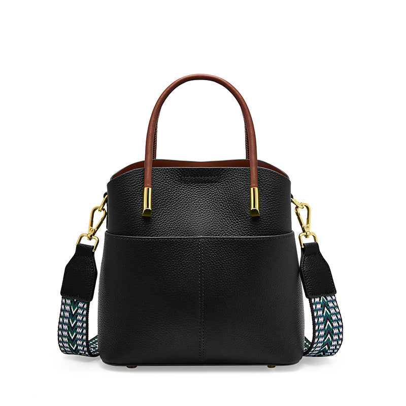 Black cowhide leather bucket bag with top handles and woven strap on white background