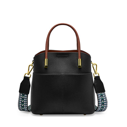 Black cowhide leather bucket bag with top handles and woven strap on white background
