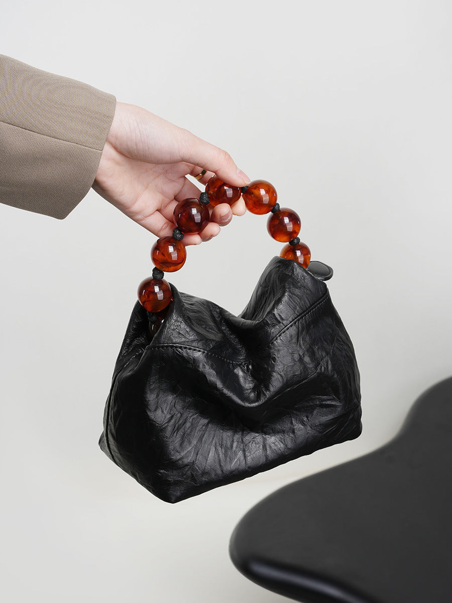 Hand holding the black crinkle leather bag by its amber bead handle