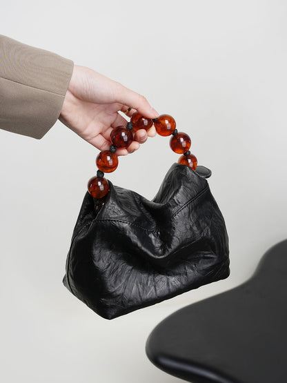 Hand holding the black crinkle leather bag by its amber bead handle