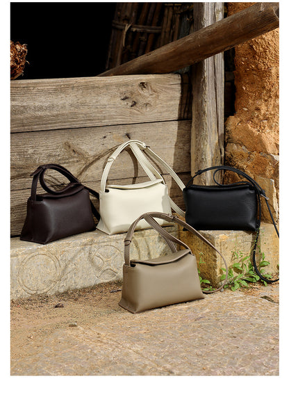 Black, white, and khaki leather crossbody bags displayed together on stone