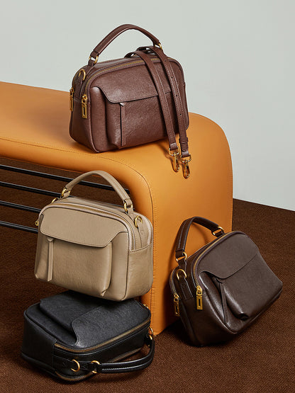 Four color variants of the Boston crossbody bag displayed on and beside an orange bench