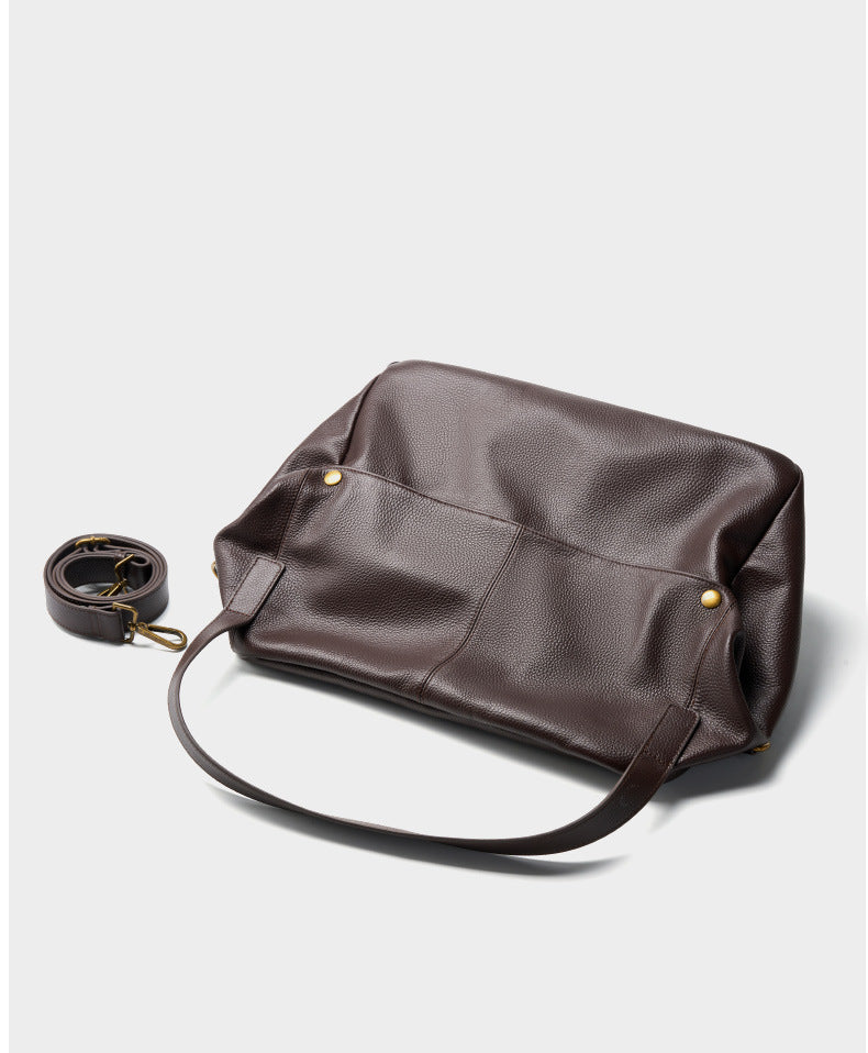 Top-down view of brown leather tote with detachable strap coiled beside it