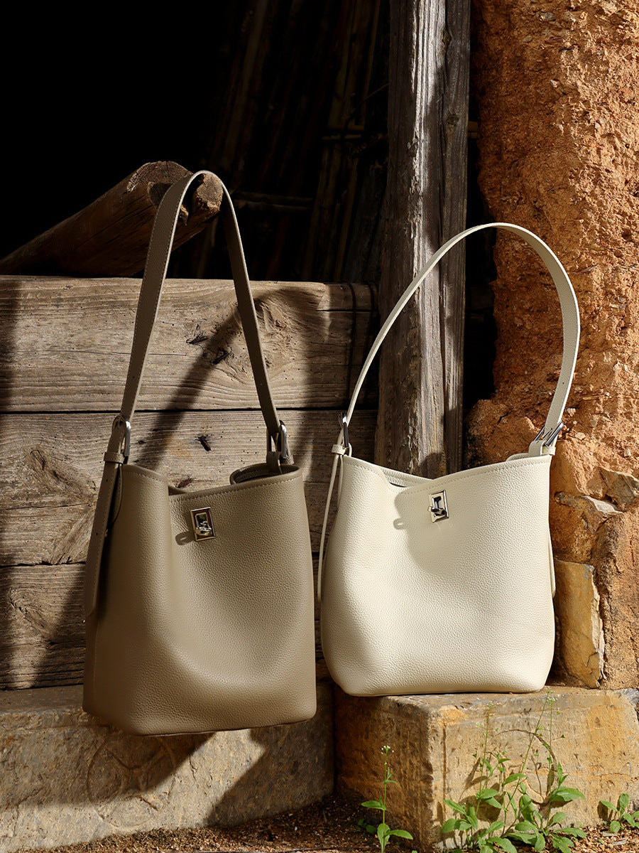 Khaki and off-white leather bucket bags sitting on a stone step next to a wooden wall