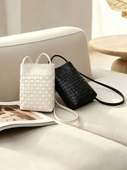 Black and cream white woven phone bags displayed on a cream sofa with magazine