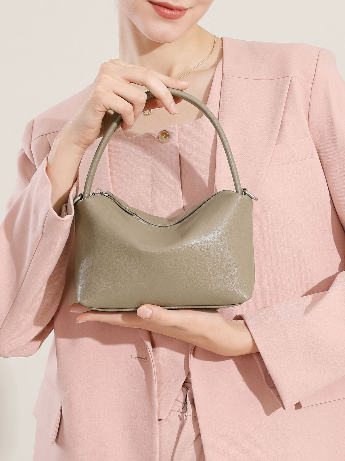 Gray top-grain cowhide pillow bag held by a model in a pink blazer