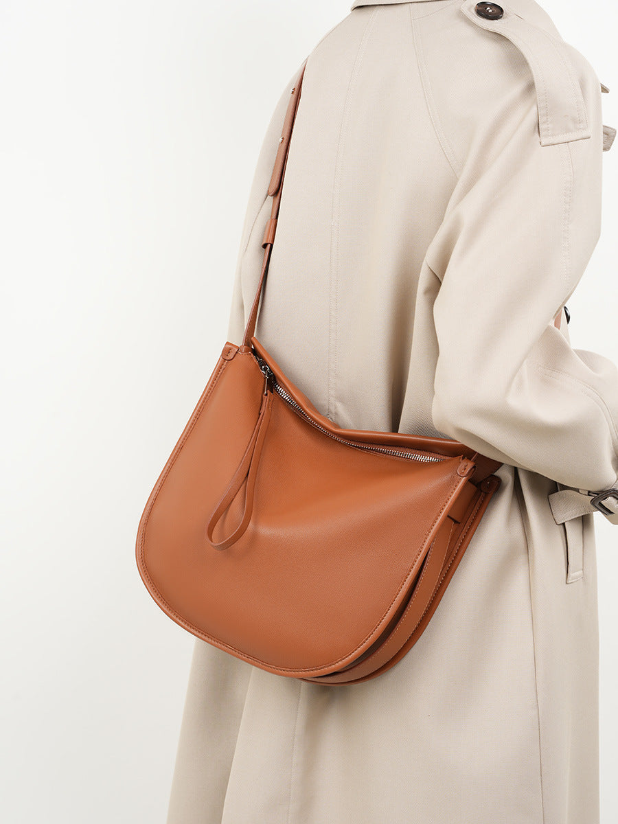 Side view of tan leather hobo bag worn on shoulder with trench coat