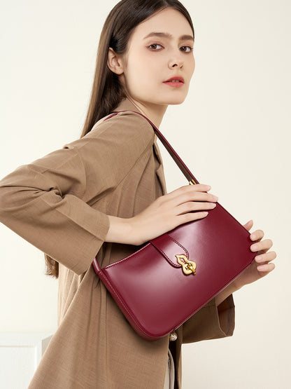 Model holding burgundy leather shoulder bag at waist in casual outfit
