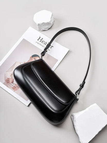 Lifestyle shot of the black leather baguette bag placed on a magazine