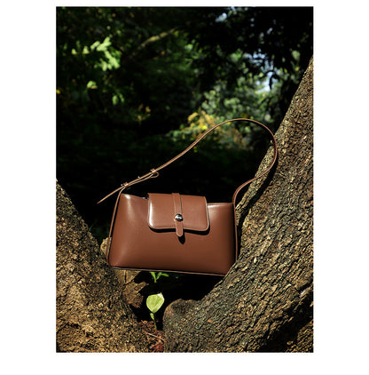 Brown leather bag hanging on tree branch close-up